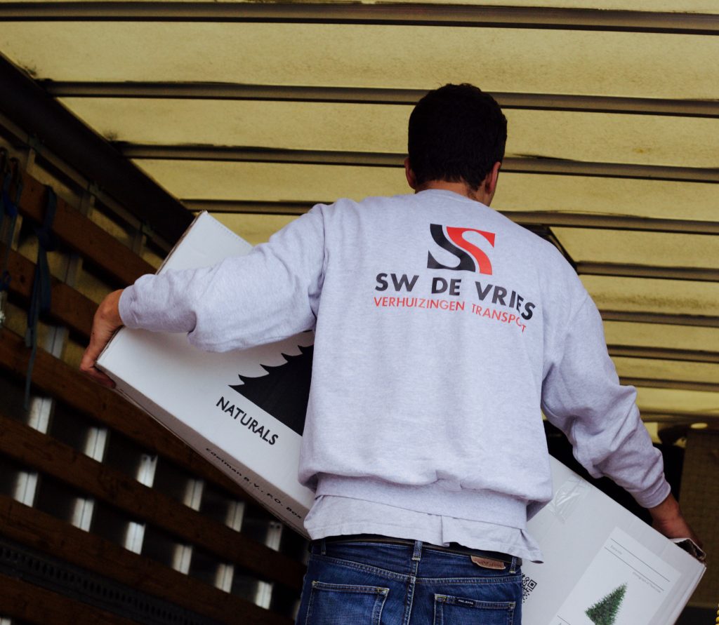 Verhuizer van SW de Vries Verhuizingen tilt een doos met kerstboom in een verhuiswagen.